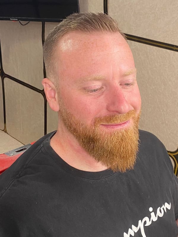 Smiling man with a freshly shaped full red beard and a short cut