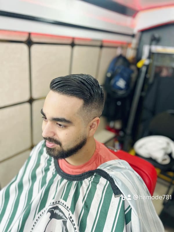 Client in a striped barber cape with a fade, swept-back top and a lined-up beard