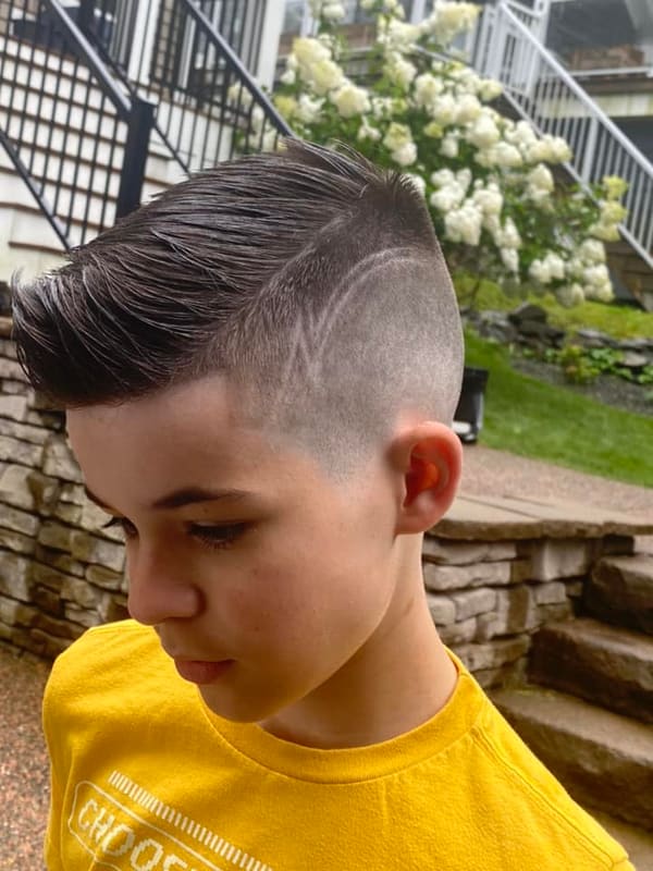 Boy in a yellow shirt with a short fade and a shaved part line, combed over on top