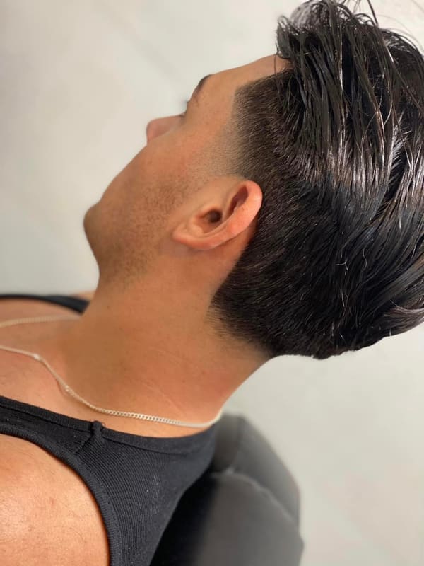 Thick dark hair swept back with length on top and a low taper at the neck