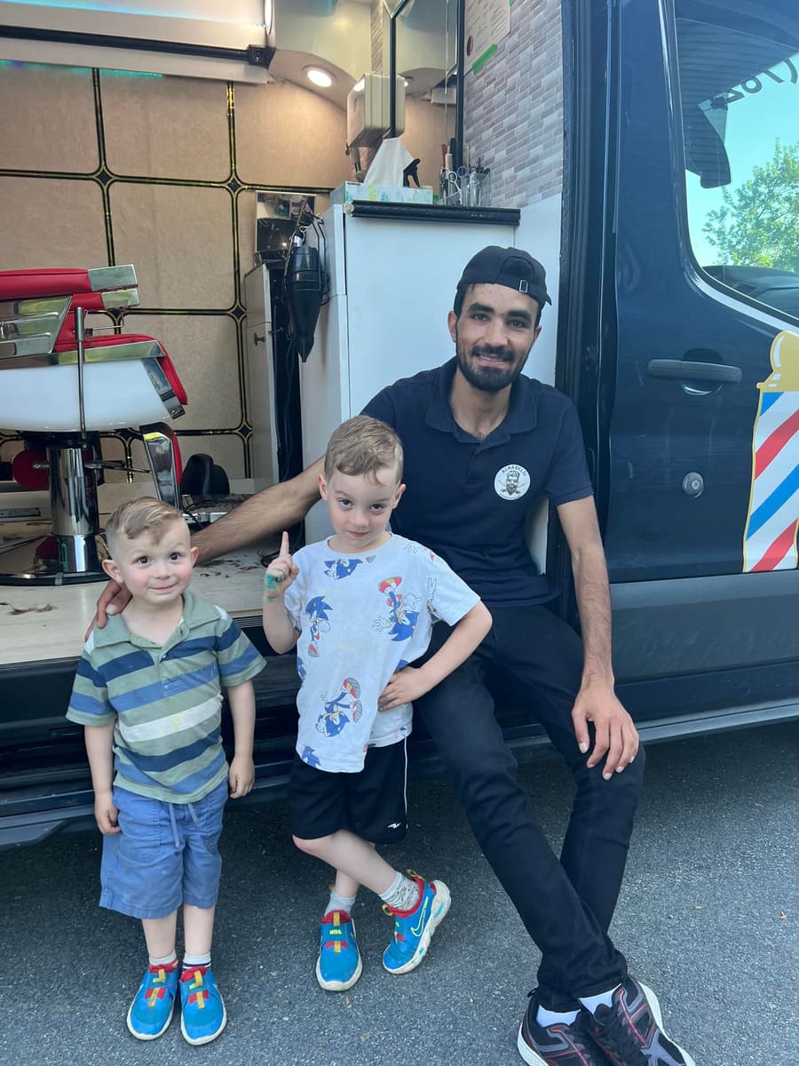 Mohammad crouching in front of the open van with two young customers