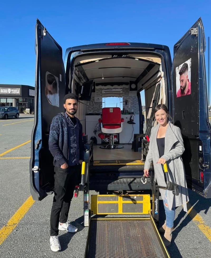 The back doors of the Alnabelsi van open with the yellow wheelchair lift lowered to the ground, two people standing beside it