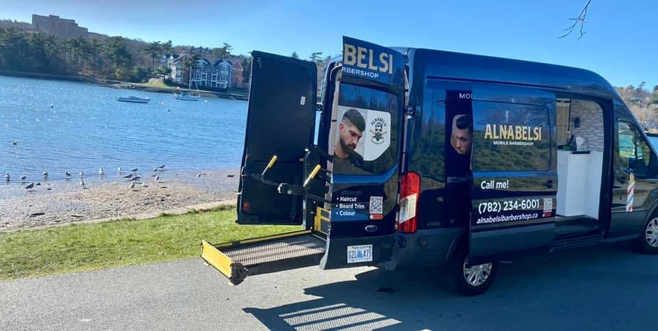 The navy Alnabelsi Barbershop van parked beside a beach with its side door open